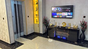 A modern lobby with a black and gold console, a TV displaying various channels, and a decorative wall with shelves. - Tobby Royal Suites (Lagos)