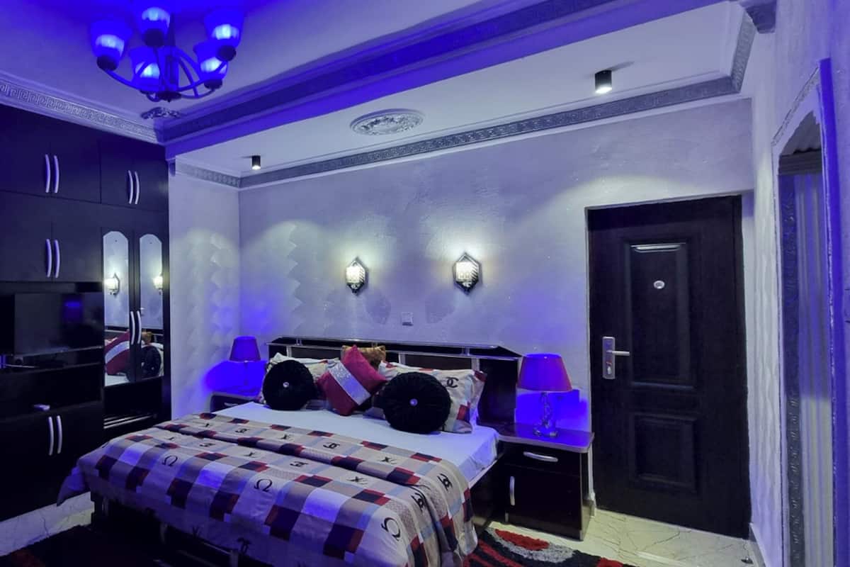 Quarto com cama, guarda-roupa, espelho e luzes na parede.