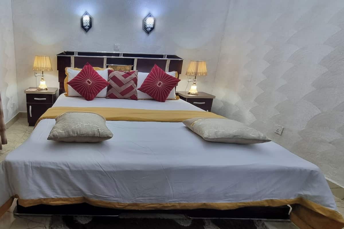 Quarto de hotel com uma cama grande, duas mesas de cabeceira com luminárias e um painel decorativo na parede.