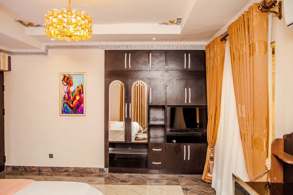 A bedroom with a large wardrobe, a bed, a TV, and a chandelier. - Tobby Royal Suites (Lagos)