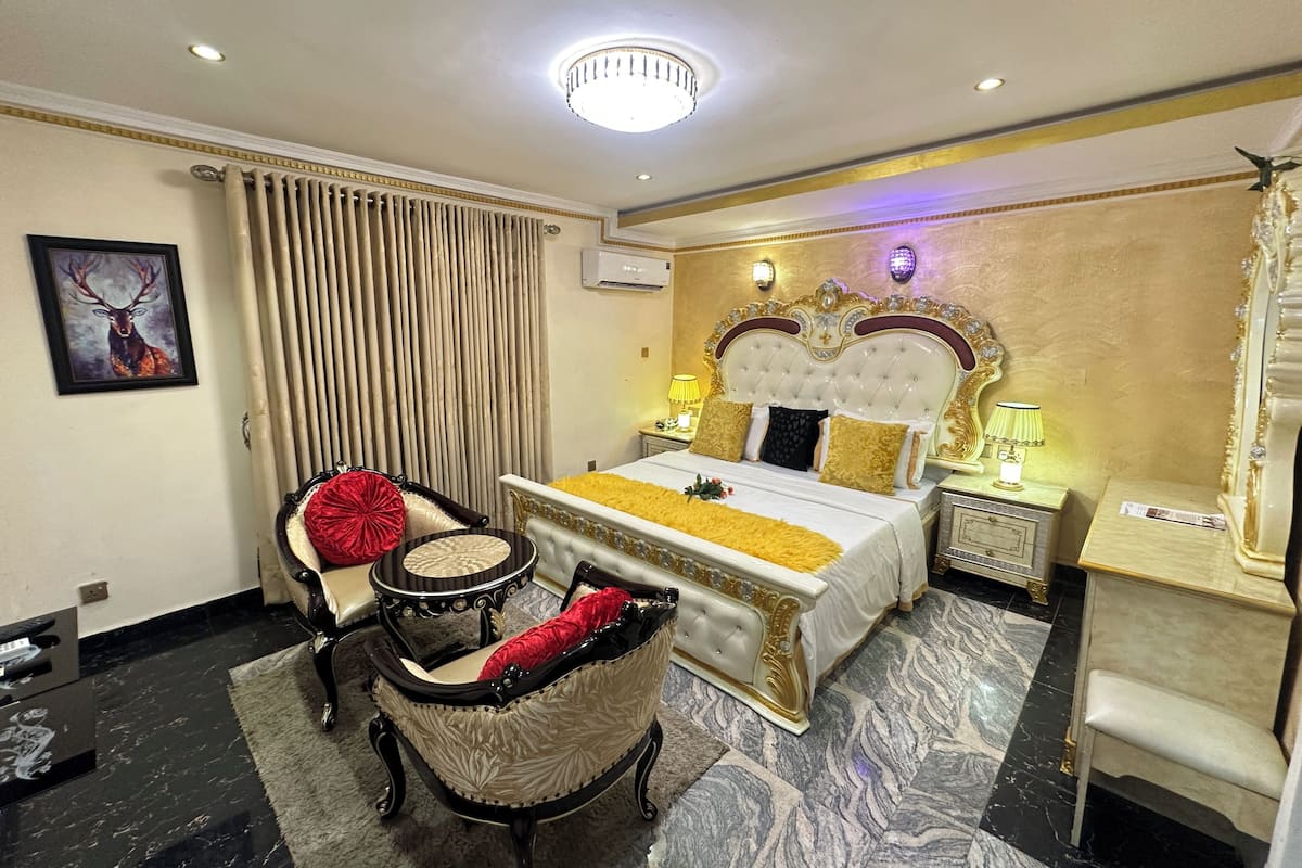 Quarto de hotel com uma cama grande, duas mesas de cabeceira, um candelabro, um quadro e uma janela com cortinas.