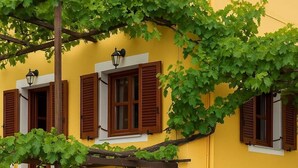 Un edificio giallo con persiane di legno e edera che ricopre le finestre, sotto un cielo sereno.