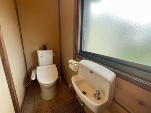 A compact bathroom with a toilet and sink, featuring a small plant and a window above the sink.