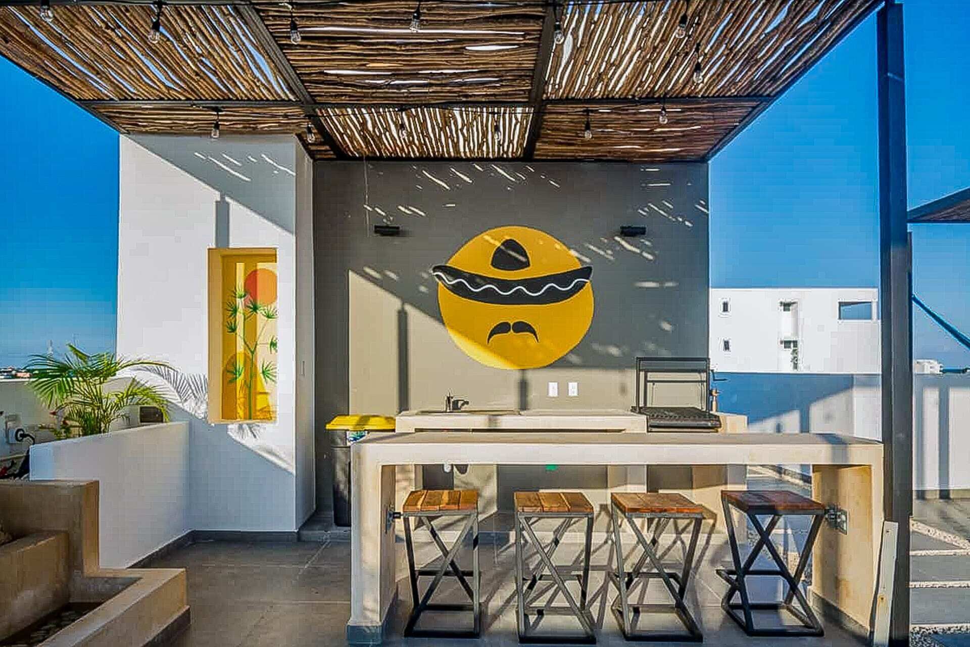 A modern outdoor kitchen area with a unique wall art piece, a bar counter, and stools.
