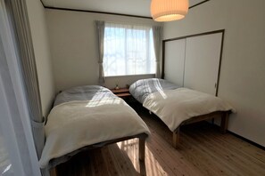 Une chambre avec deux lits simples, un plancher en bois, une fenêtre avec des rideaux et une armoire.