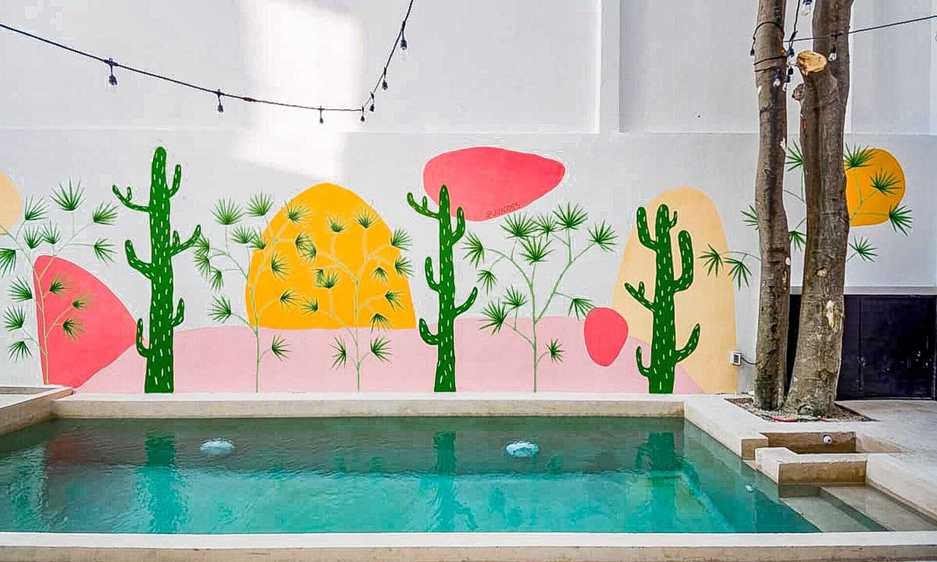 Una piscina con un mural colorido en la pared, un árbol y una guirnalda de luces.