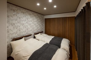 A bedroom with two beds, wooden wardrobe, floral wallpaper, and a curtain.
