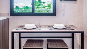 A dining area with a table and benches, a window with a view of greenery, and a wall-mounted TV. - Stylish Condo - Pool + Rooftop - Walk to 5th Ave (Playa del Carmen)