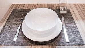 A dining table set with a plate, fork, knife, and glass, positioned in front of a window with a view of greenery and buildings. - Stylish Condo - Pool + Rooftop - Walk to 5th Ave (Playa del Carmen)