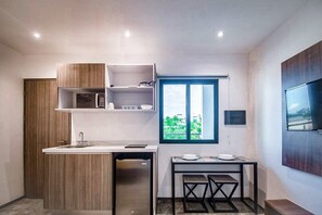 A compact kitchen with a built-in microwave, a small sink, and a dining area with a table and chairs. - Playa del Carmen Escape - Pool and Rooftop (Playa del Carmen)