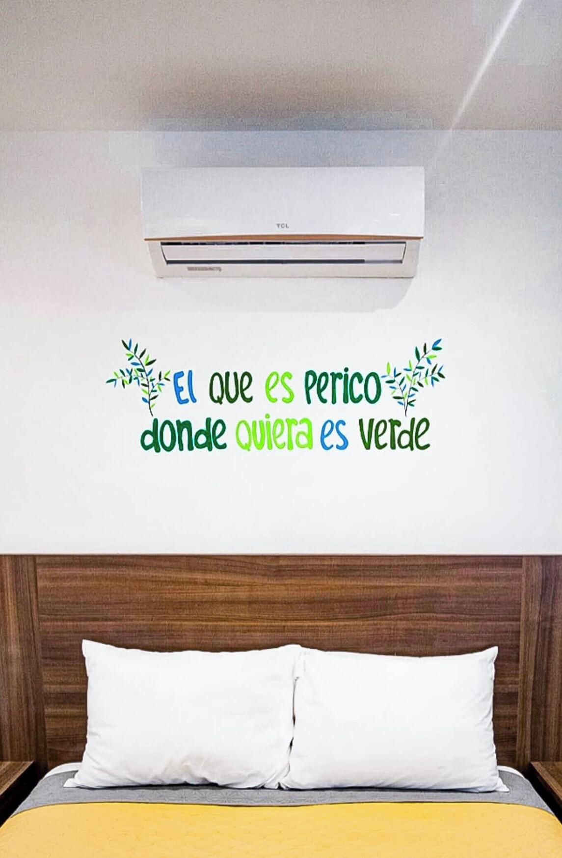 Quarto de hotel com cama, almofadas brancas, cabeceira de madeira e ar condicionado fixado na parede.