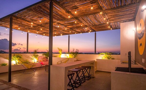 Un espace extérieur aménagé en terrasse, doté d’un toit de chaume, de guirlandes lumineuses et de sièges.