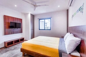 Une chambre à coucher avec un lit, un téléviseur fixé au mur, une fenêtre et un ventilateur de plafond.