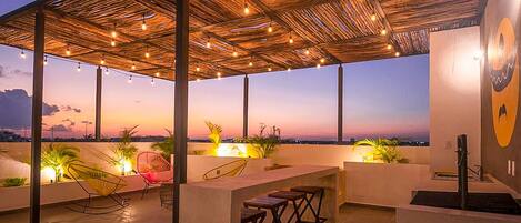 An outdoor patio area with a thatched roof, string lights, and bar stools.