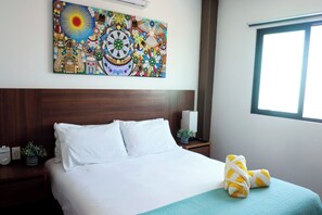 A hotel room with a large bed, a nightstand with a lamp, a wall-mounted artwork, and a window.