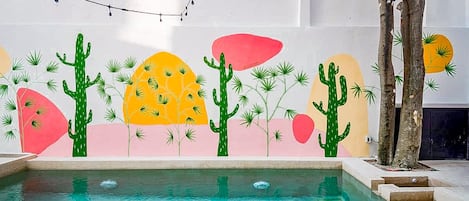 A swimming pool with a colorful mural on the wall, a tree, and a string of lights.