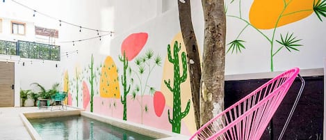 A pool area with a mural of cacti and palm trees, a pink chair, and string lights.