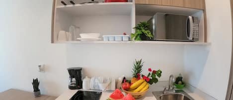 A compact kitchen with a microwave, a red pot, a coffee maker, and a fruit bowl.