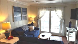 Ein Wohnzimmer mit einer Couch, einem kleinen Tisch, einem Fernseher und einem Fenster mit Vorhängen.