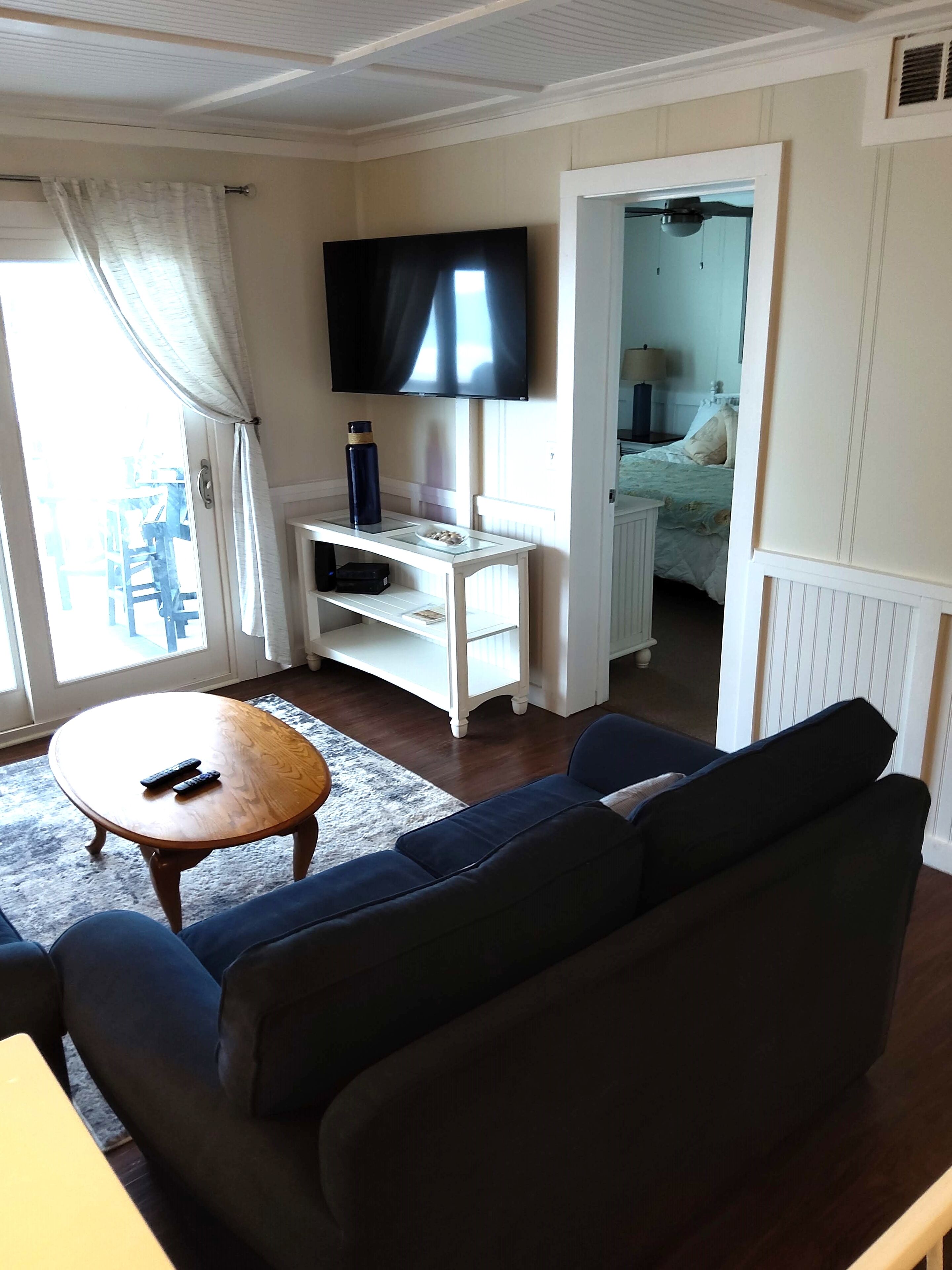 En stue med en sofa, et sofabord, et fjernsyn på et stativ og en dør, der fører til et soveværelse.