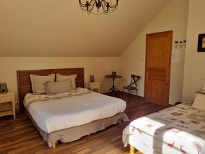A bedroom with a large bed, a bedside table, a small table with a chair, and a wooden door.