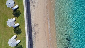 Luchtbeeld van een strand met helder turquoise water, een zandstrand en meerdere ligbedden met parasols.