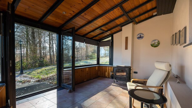 Ein modernes Interieur mit einer großen Glasdoor, die zu einer Waldlandschaft führt, einem Kamin und einer Sitzecke.