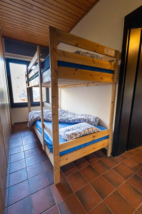 A bunk bed with a patterned bedspread and pillows, wooden headboard, and a window with a view.