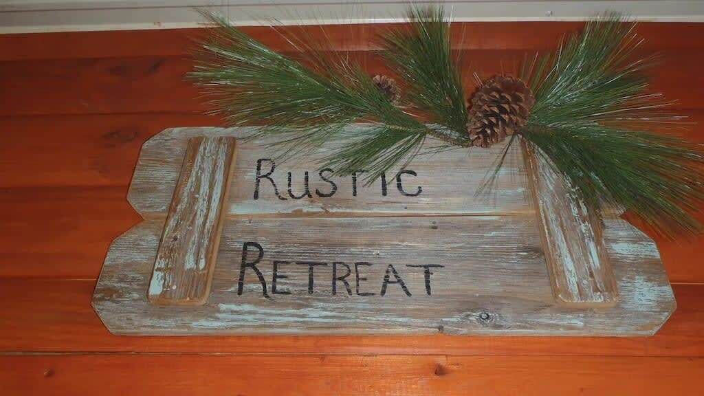Letrero de un refugio rústico con ramas de pino y una decoración de piñón.