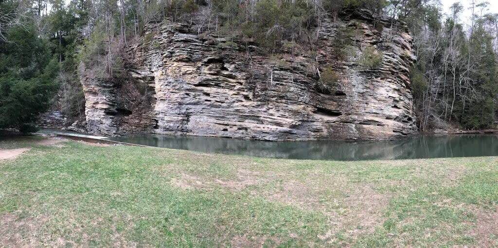 A natural landscape with a rocky cliff and a calm body of water.