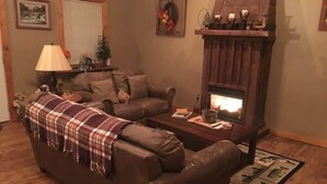 Un salon chaleureux avec une cheminée, un canapé en cuir marron et une couverture à carreaux.