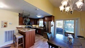 Een keuken met een centraal eiland, houten kasten, roestvrijstalen apparatuur en een eetgedeelte met een tafel en stoelen.