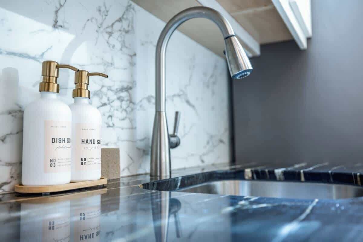 A bathroom with a marble countertop, a modern faucet, and two bottles labeled "DISH SOAP" and "HAND SOAP".