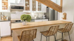 Eine moderne Küche mit weißen Schränken, einer Holz-Kochinsel, Korbstühlen und einem Edelstahl-Kühlschrank.