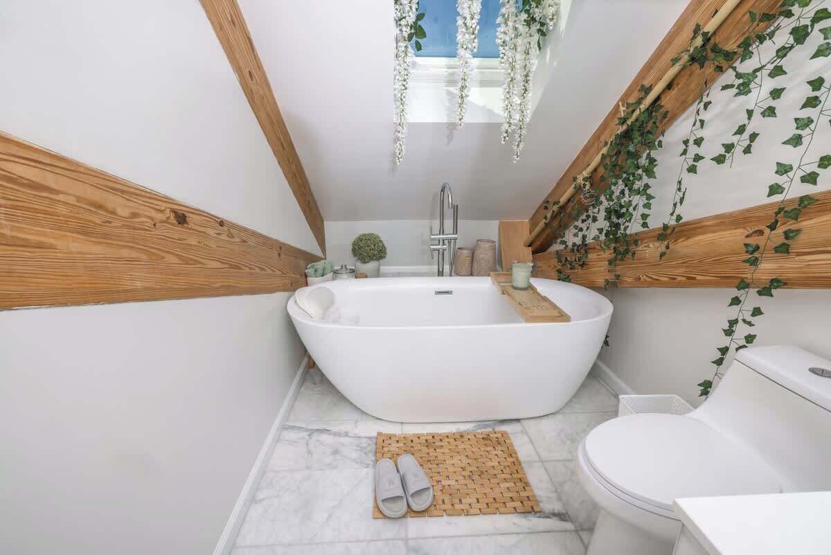 A modern bathroom with a freestanding bathtub, wooden beams, and hanging greenery.
