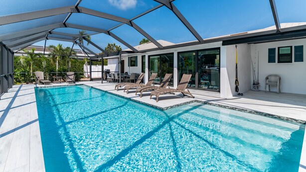 Ein Schwimmbecken mit Liegestühlen, einer überdachten Terrasse und Blick auf die Umgebung.