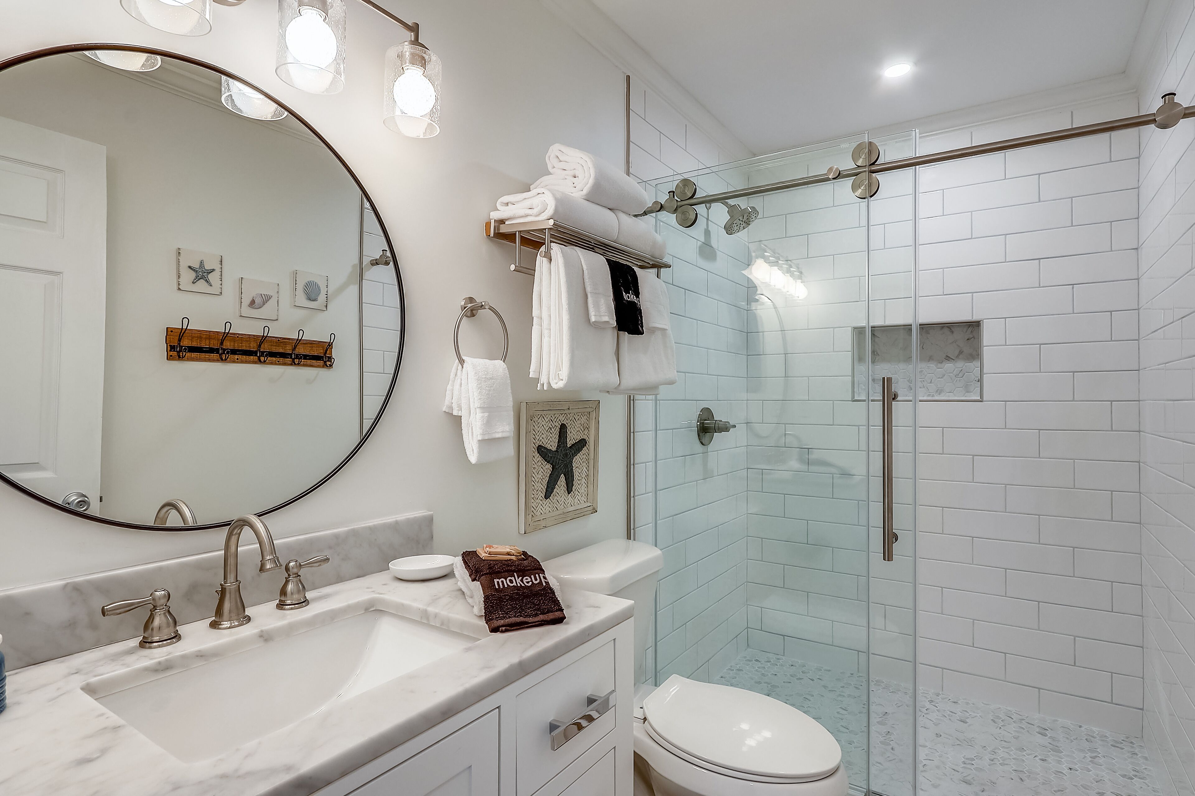 A modern bathroom with a large mirror, a sink with three faucets, a toilet, and a glass-enclosed shower area.