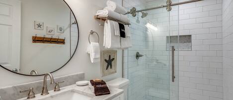A modern bathroom with a large mirror, a sink with three faucets, a toilet, and a glass-enclosed shower area.