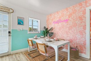 A dining area with a white table, chairs, and a wall with a tropical leaf pattern.