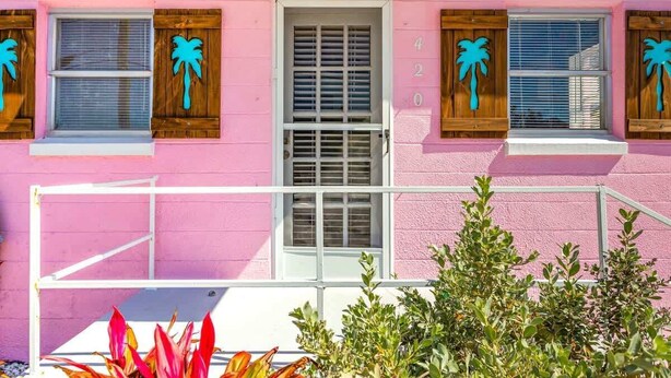 Ein rosafarbenes Gebäude mit Fensterläden, einer Tür und einem Balkon.
