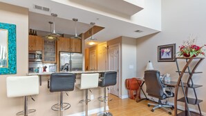 A modern kitchen with bar stools, a dining area with a chair and a desk, and a staircase leading to another level. - One Bedroom Hideaway w/ free parking steps to Downtown (Raleigh)