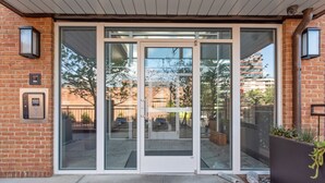 A modern building entrance with glass doors, a keypad, and a small outdoor area with plants. - One Bedroom Hideaway w/ free parking steps to Downtown (Raleigh)