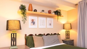 A neatly arranged bedroom with a bed, bedside lamps, a nightstand, a dresser, and a shelf with decorative items. - One Bedroom Hideaway w/ free parking steps to Downtown (Raleigh)