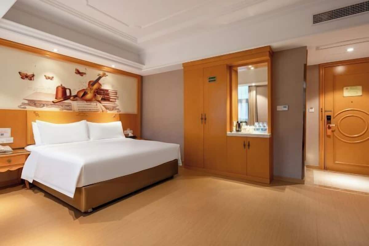 Ein Hotelzimmer mit einem großen Bett, einem Holzschrank und einem an der Wand befestigten Kunstwerk.