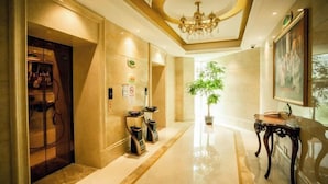 A hotel lobby with a marble floor, a chandelier, a potted plant, and a coat rack. - Vienna Hotel (Shanghai Chongming Lvhai Road) (Shanghai)