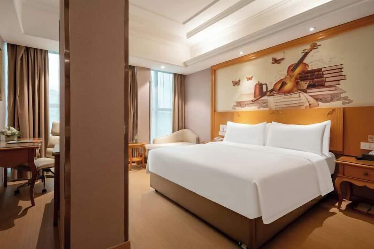 Ein Hotelzimmer mit einem großen Bett, einem Schreibtisch mit Stuhl, einem Nachttisch und einer Wand mit Wandmalerei.