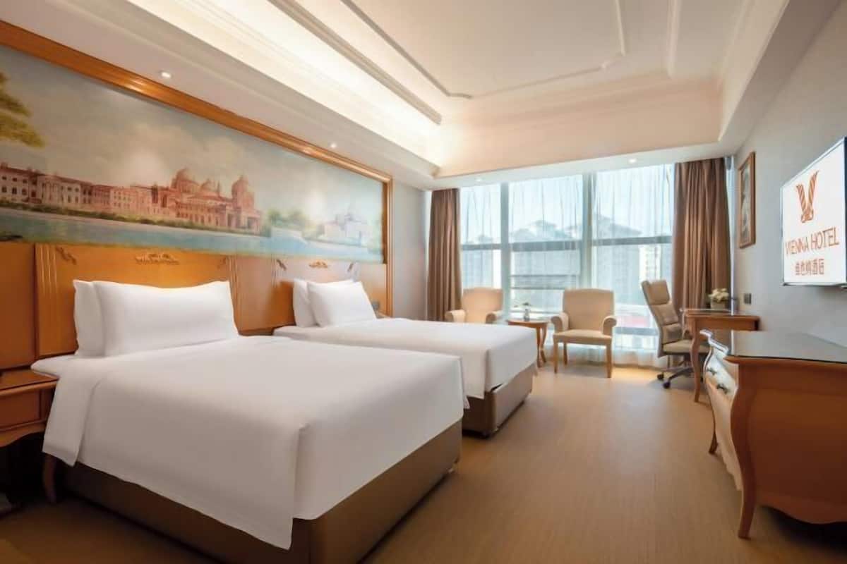 Ein Hotelzimmer mit zwei Betten, einem Schreibtisch, einem Stuhl und einem großen Fenster.