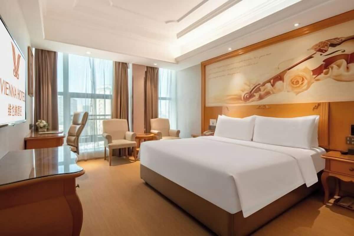 Ein Hotelzimmer mit einem großen Bett, einem Schreibtisch, einem Sessel, einem kleinen Tisch und einem großen Fenster.