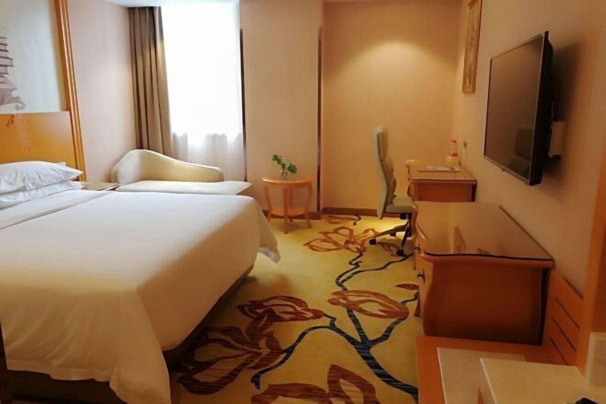 A hotel room with a bed, a chair, a small table, a TV, and a floral carpet.