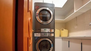 A stacked washer and dryer unit in a kitchen with cabinets and a basket on the countertop. - Vienna Hotel (Shanghai Chongming Lvhai Road) (Shanghai)